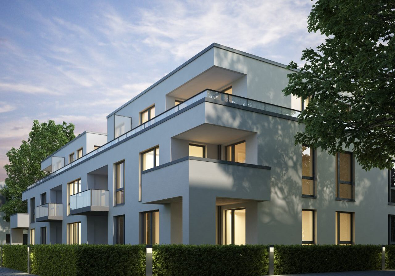 Modern apartment building with large windows, multiple balconies, and flat roof, surrounded by green hedges and trees, under a partly cloudy sky during dusk or dawn.